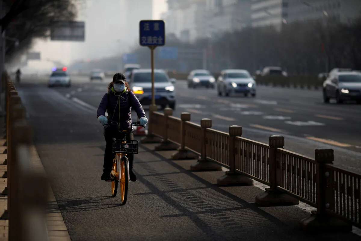 A woman wearing a face mask rides a shared bicycle on a main road in central Beijing in the morning after the extended Lunar New Year holiday caused by the novel coronavirus outbreak, on Feb. 10, 2020. (Carlos Garcia Rawlins/Reuters)
