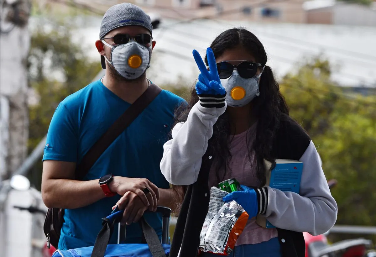A woman shows the peace hand sign as she and her companion cautiously travel through Toncontin International Airport in Tegucigalpa, Honduras, on March 12, 2020. (Orlando Sierra/AFP via Getty Images)
