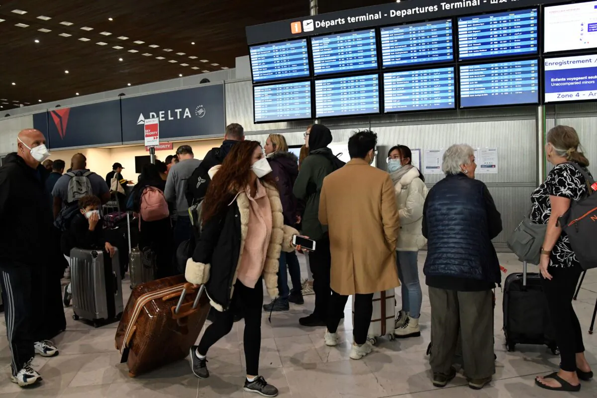 A traveler with a face mask passes by other standing in front of screens displaying flight schedules at the Paris airport after U.S. President Donald Trump announced a travel ban over the new coronavirus, on March 12, 2020. (Bertrand Guay/AFP via Getty Images)