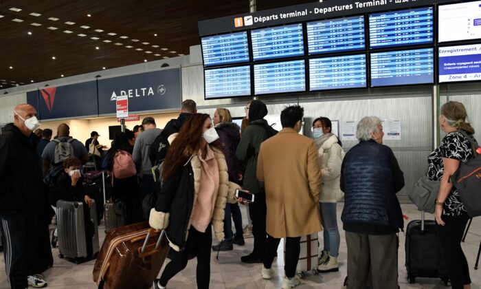 A traveler with a face mask passes by other standing in front of screens displaying flight schedules at the Paris airport after U.S. President Donald Trump announced a travel ban over the new coronavirus, on March 12, 2020. (Bertrand Guay/AFP via Getty Images)