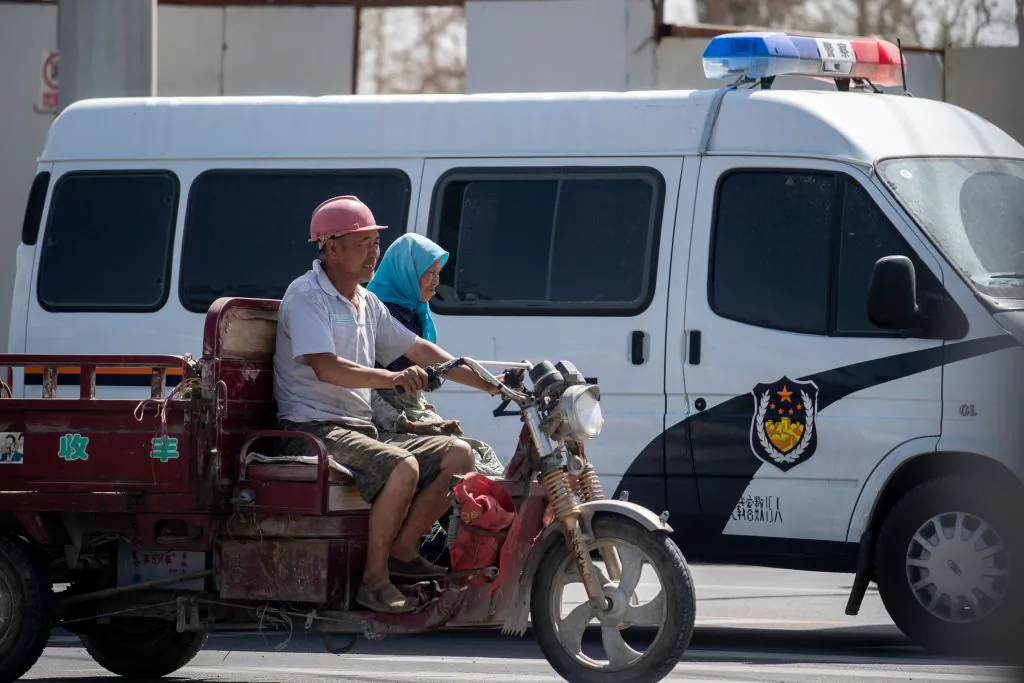 Local Muslims pass a police car in their vehicle in Hotan in China's Xinjiang Uighur Autonomous Region on June 23, 2017. (Johannes Eisele/AFP via Getty Images)