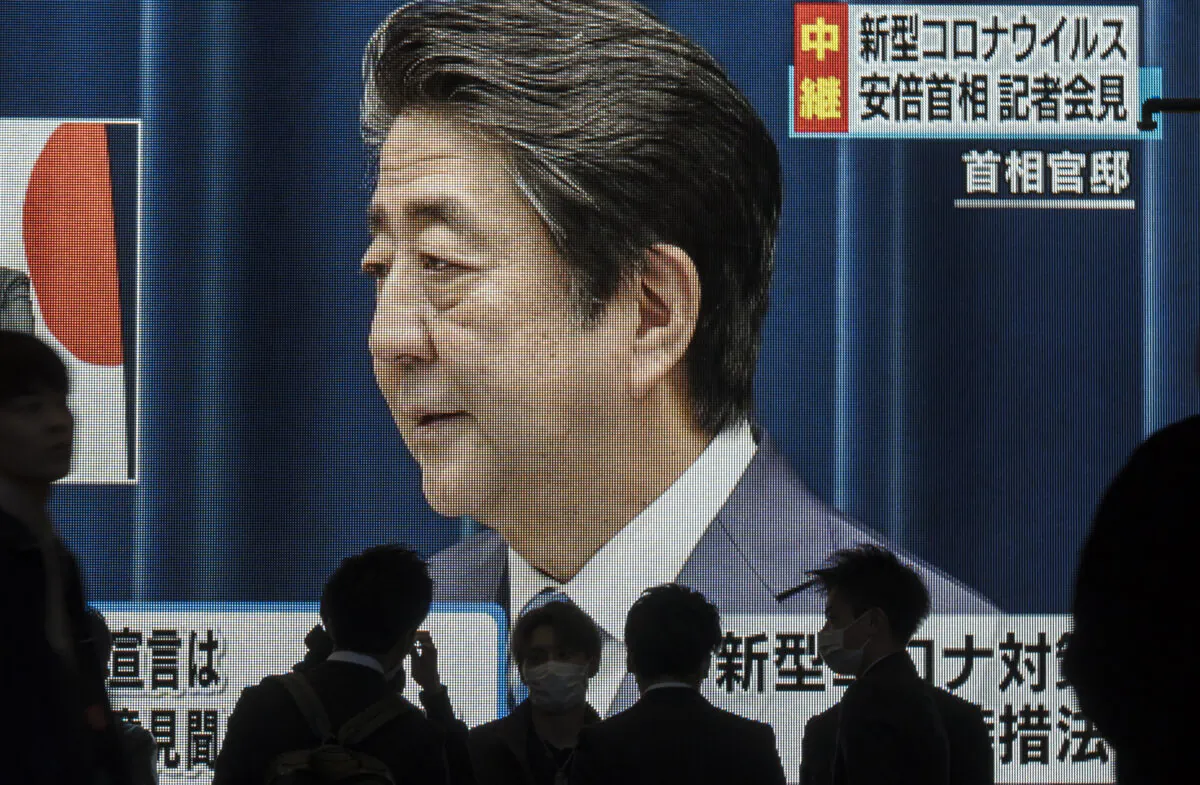 Pedestrians walk past a monitor showing a live broadcast of a press conference by Japanese Prime Minister Shinzo Abe on COVID-19 in Osaka, Japan, on March 14, 2020. (Tomohiro Ohsumi/Getty Images)