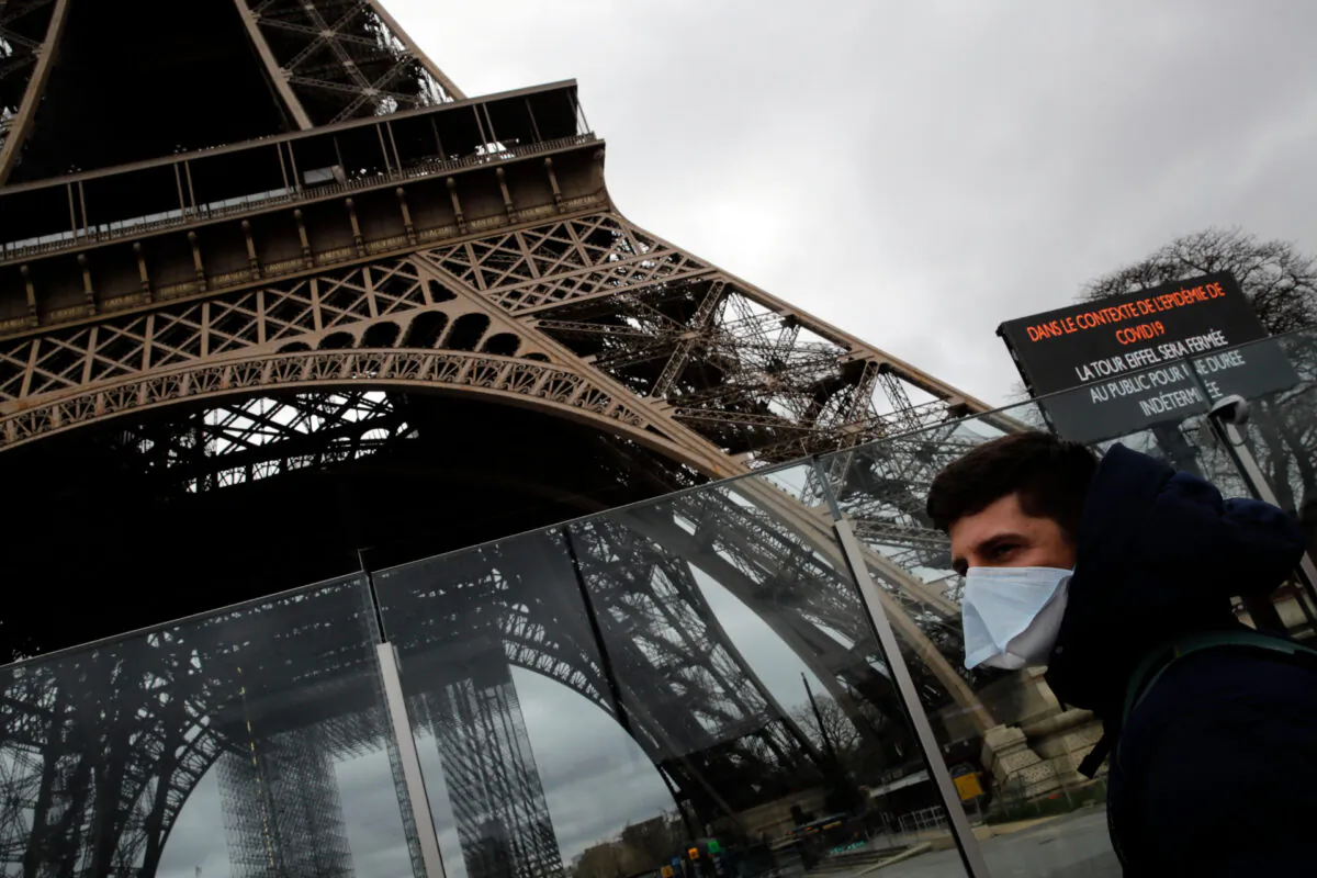 A man wearing a mask walks pasts the Eiffel tower closed after the French government banned all gatherings of over 100 people to limit the spread of the virus COVID-19, in Paris, on March 14, 2020. (AP Photo/Christophe Ena)