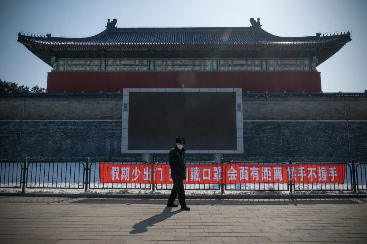 A security guard walks past a propaganda banner saying, "Do Not Leave Home Often During Holidays, Wear a Mask When Going Out, Keep a Distance and Do Not Shake Hands When Meeting" in Temple of Heaven Park, Beijing on Feb. 15, 2020. (Andrea Verdelli/Getty Images)