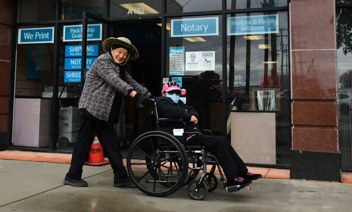 An elderly woman wears a face mask as a precaution against COVID-19, coronavirus, while being pushed in her wheelchair in Monterey Park, Calif., on March 10, 2020. (Frederic J. Brown/AFP via Getty Images)