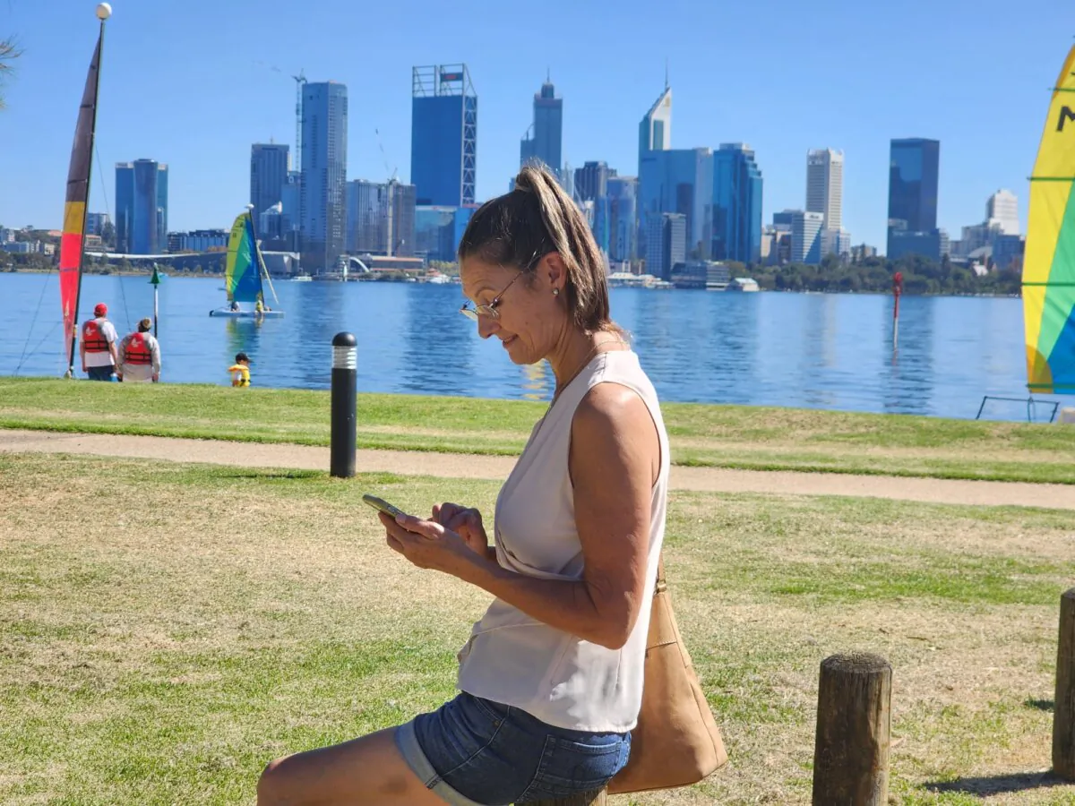 A woman looks at her mobile phone on the banks of the Swan River in South Perth, Western Australia, on March 16, 2024. (Susan Mortimer/The Epoch Times)