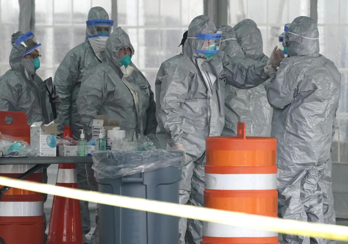 Workers in protective suits wait for people to be tested for Coronavirus (COVID-19) as they arrive by car at the state's first drive-through COVID-19 Mobile Testing Center at Glen Island Park in New Rochelle, N.Y., March 13, 2020. (Timothy A. Clary/AFP via Getty Images)