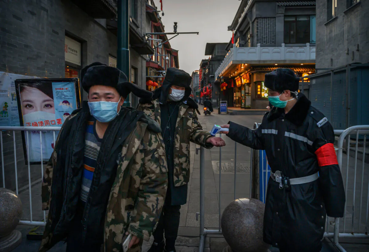 A Chinese man wears a protective mask as he and others have their temperature checked by a guard at a temporary entrance to a commercial area in Beijing on March 11, 2020. (Kevin Frayer/Getty Images)