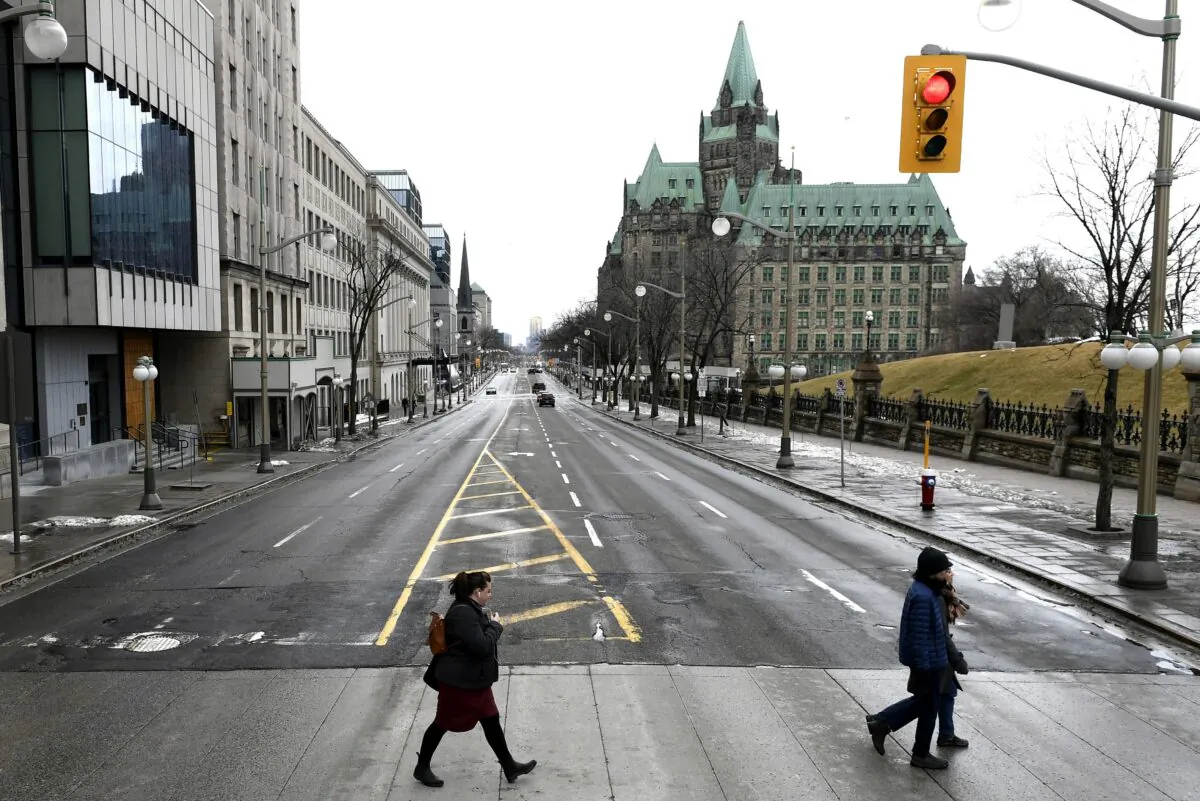 People cross a largely deserted Wellington Street, the major street in front of Parliament Hill in Ottawa, on March 17, 2020. (The Canadian Press/Justin Tang)