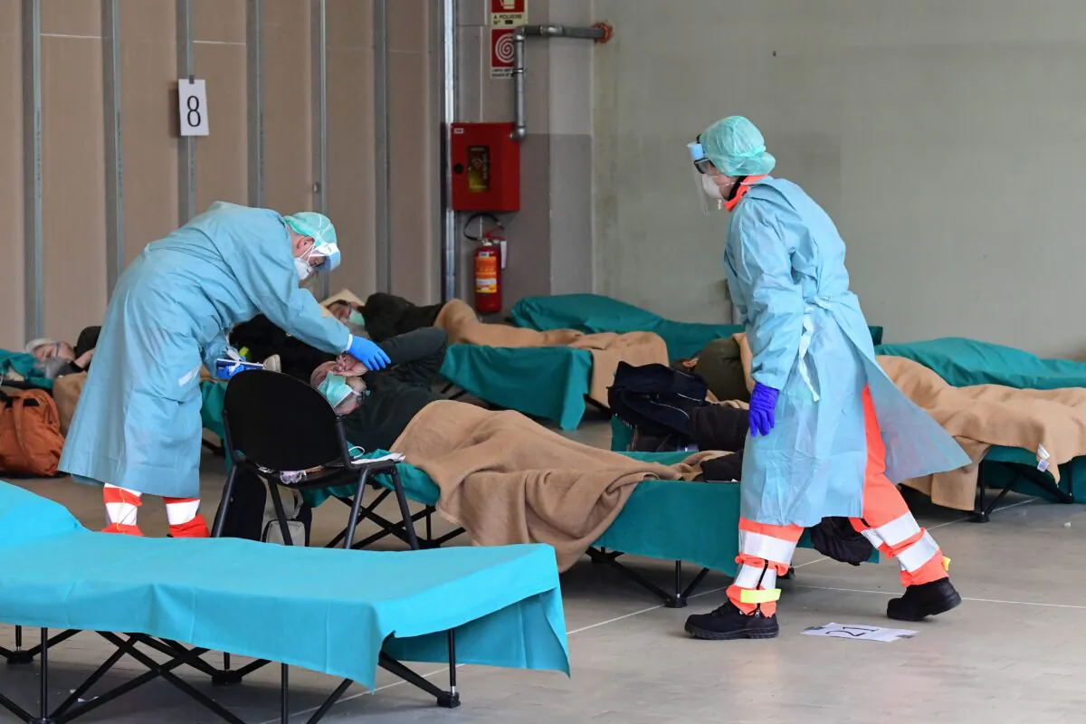 Hospital employees attend to a patient at a temporary emergency structure set up outside the emergency department at the Brescia Hospital in Lombardy, Italy, on March 13, 2020. (Miguel Medina/ AFP)