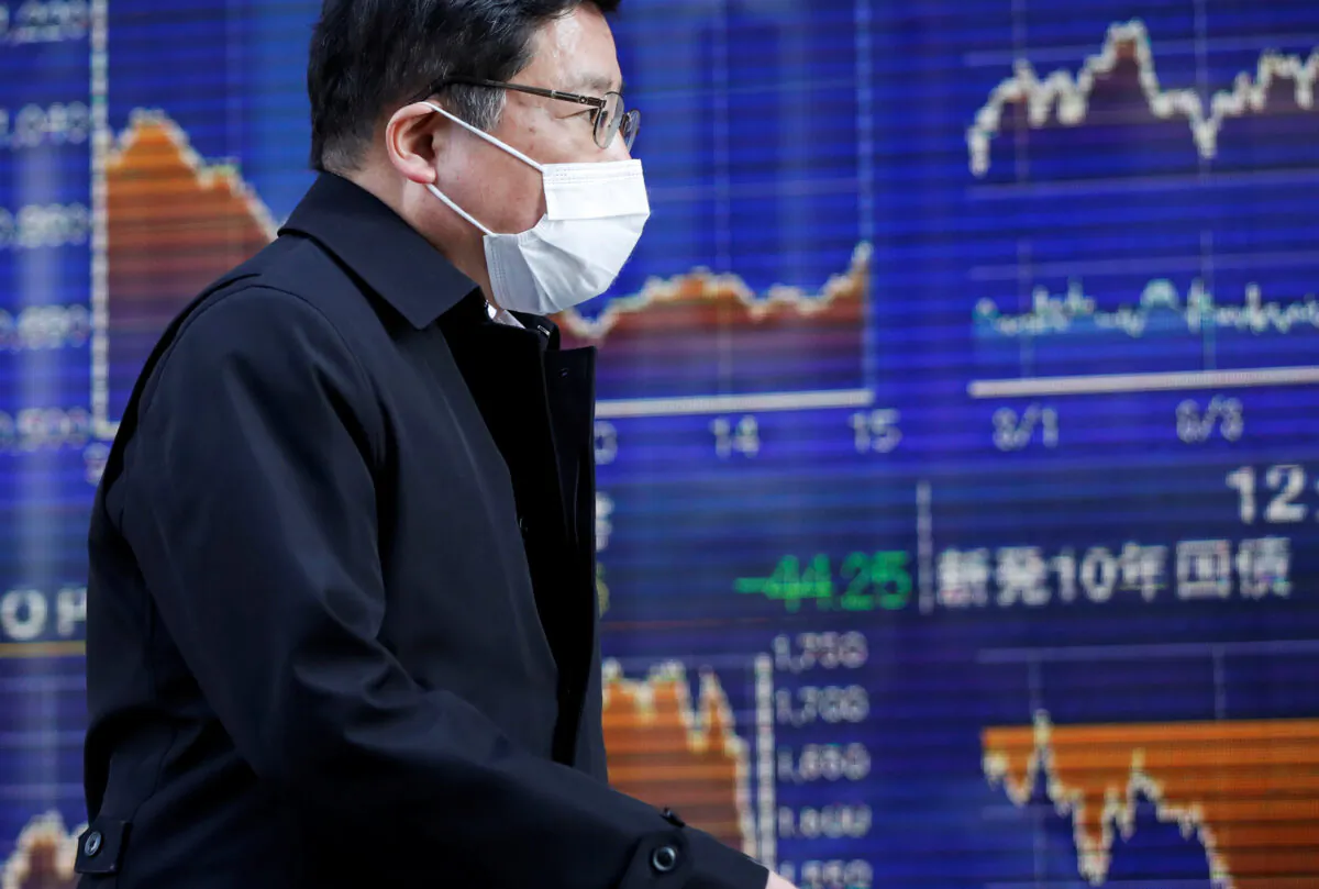 A passerby wearing a protective mask, following an outbreak of the coronavirus, walks past an electronic board showing the graphs of the recent movements of Japan's Nikkei share average outside a brokerage in Tokyo on March 6, 2020. (Issei Kato/Reuters)