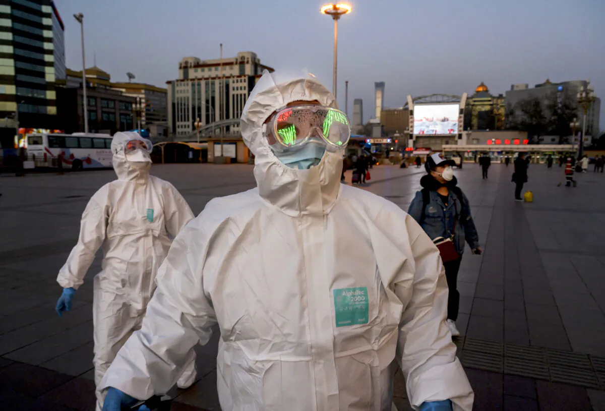 Two persons wearing protective masks and suits arrive at Beijing Railway Station on March 13, 2020.   (Kevin Frayer/Getty Images)