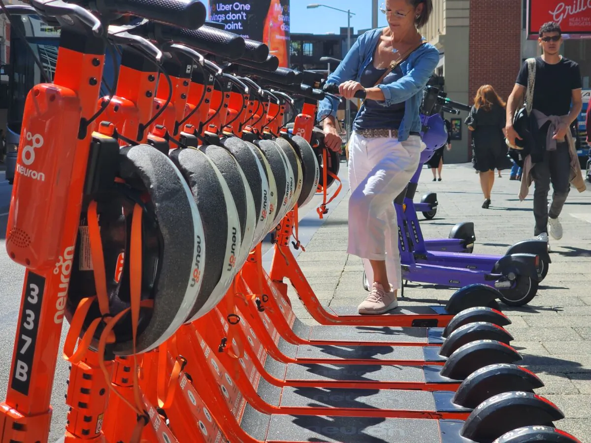 A woman grabs an electric scooter for hire in Perth, Western Australia, on March 18, 2024. (Susan Mortimer/The Epoch Times)