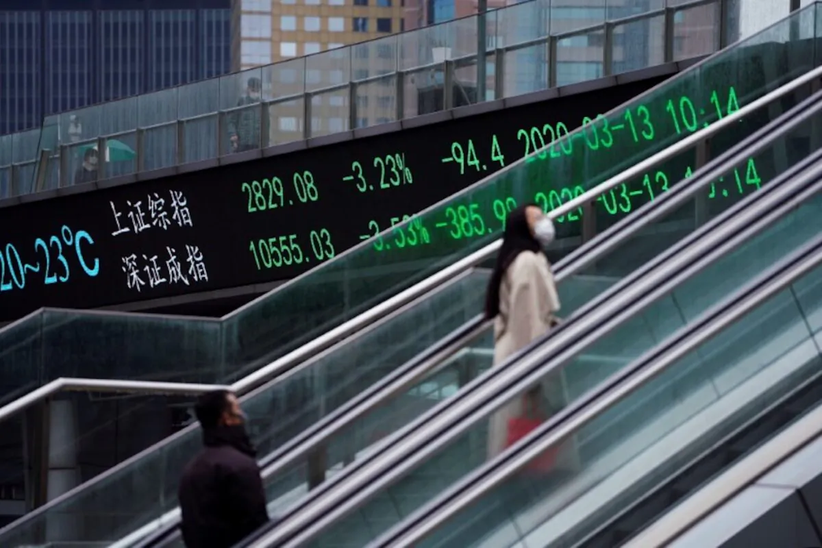 Pedestrians wearing face masks ride an escalator near an overpass with an electronic board showing the Shanghai and Shenzhen stock indexes, following an outbreak of the novel coronavirus in the country, at Lujiazui financial district, in Shanghai, China, on March 13, 2020. (Aly Song/Reuters)