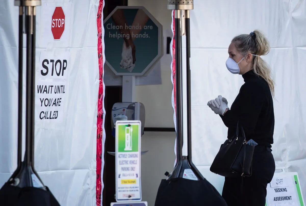 A woman wearing a protective face mask and gloves waits at a COVID-19 assessment centre for staff at Lions Gate Hospital in North Vancouver on March 19, 2020. (The Canadian Press/Darryl Dyck)