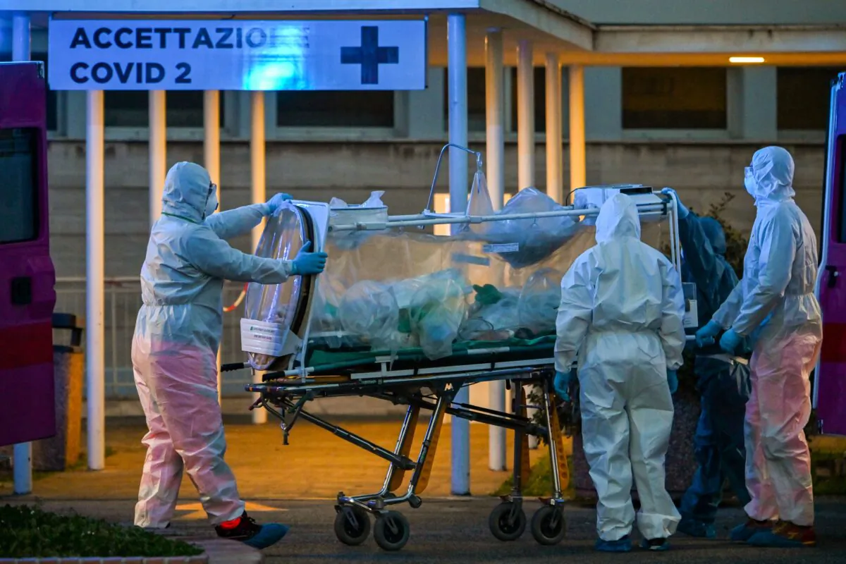 Medical workers in coveralls wheel a patient under intensive care into the newly built Columbus Covid 2 temporary hospital to fight the CCP virus, at the Gemelli hospital in Rome on March 16, 2020. (Andreas Solaro /AFP via Getty Images)