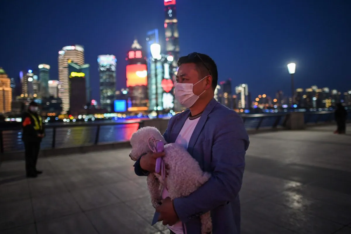 A man wearing a face mask amid concerns over the CCP virus outbreak walks holding his dog along the promenade of the Bund along Huangpu River in Shanghai, China, on March 20, 2020. (Hector Retamal/AFP via Getty Images)