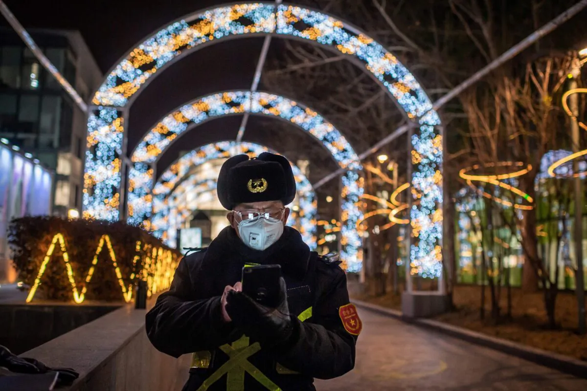 A security guard reads his cellphone while securing the entrance of a nearly empty shopping mall in Beijing, China, on Feb. 27, 2020. (NICOLAS ASFOURI/AFP via Getty Images)