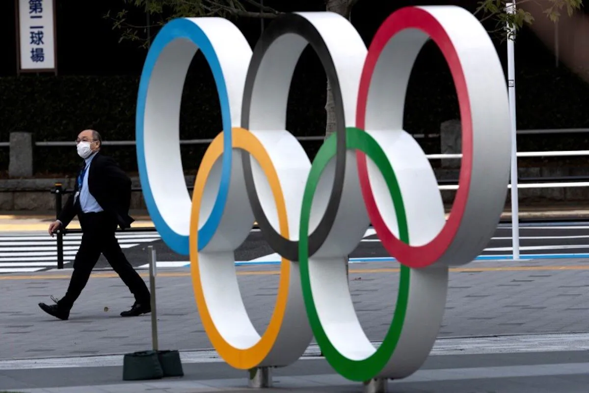 A man wearing a mask walks past the Olympic rings in front of the Japan Olympics Museum in Tokyo on March 13, 2020. (Athit Perawongmetha/Reuters)