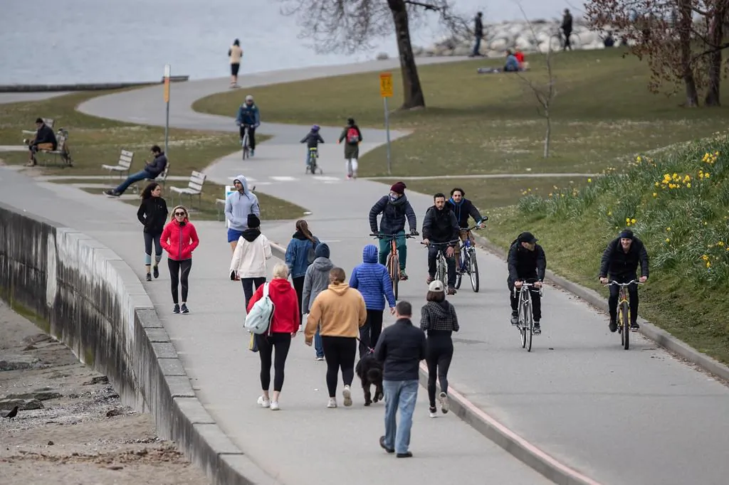 People walk and cycle on the seawall between English Bay and Sunset Beach in Vancouver on March 22, 2020. (Darryl Dyck/The Canadian Press)