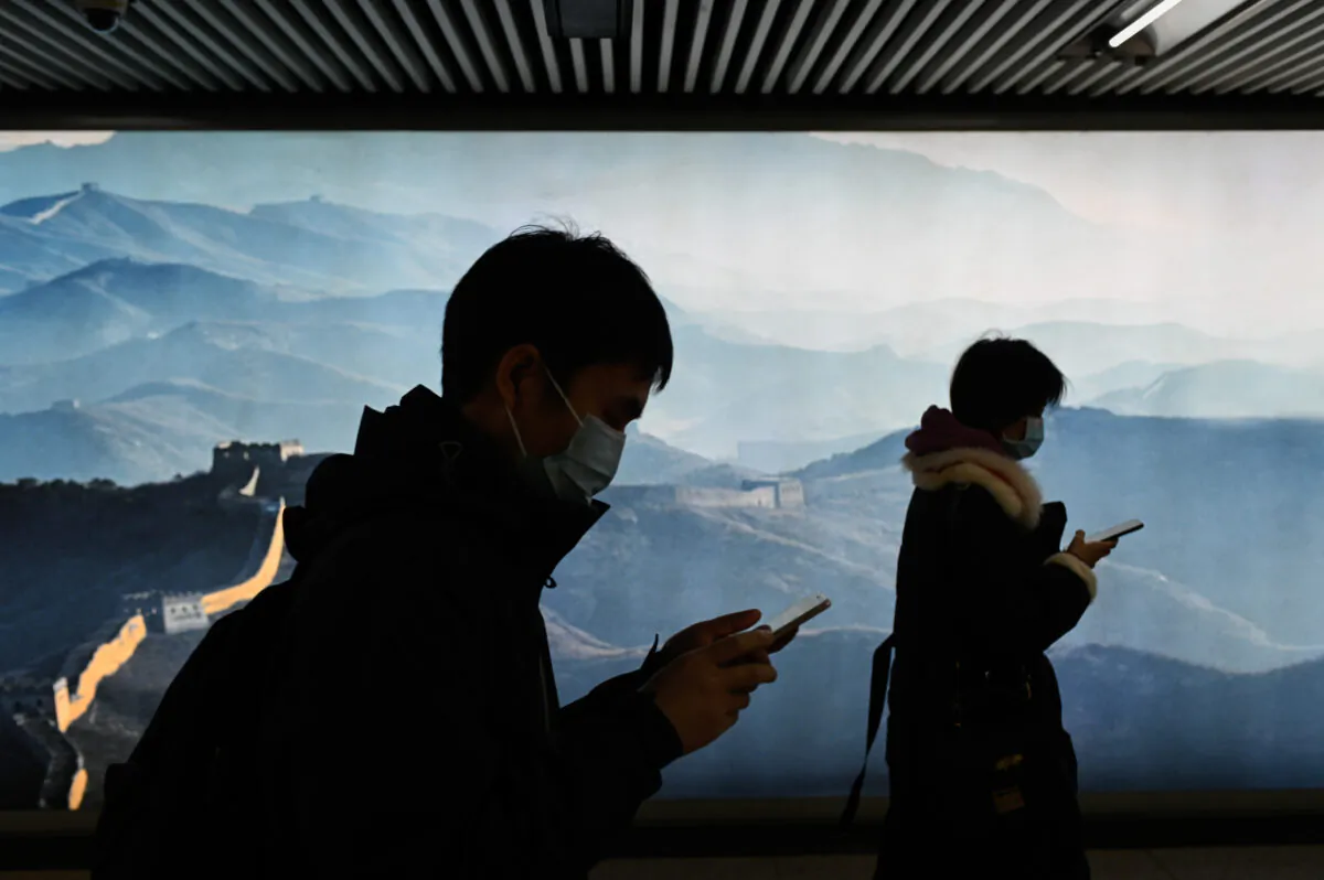 A man and a woman wearing face masks use their mobile phone as they walk in a subway station in Beijing on March 11, 2020. (Wang Zhao/AFP via Getty Images)