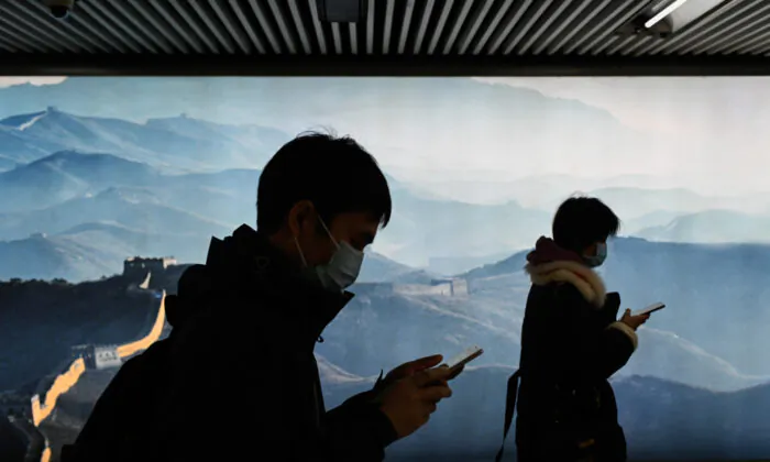 A man and a woman wearing face masks use their mobile phone as they walk in a subway station in Beijing on March 11, 2020. (Wang Zhao/AFP via Getty Images)