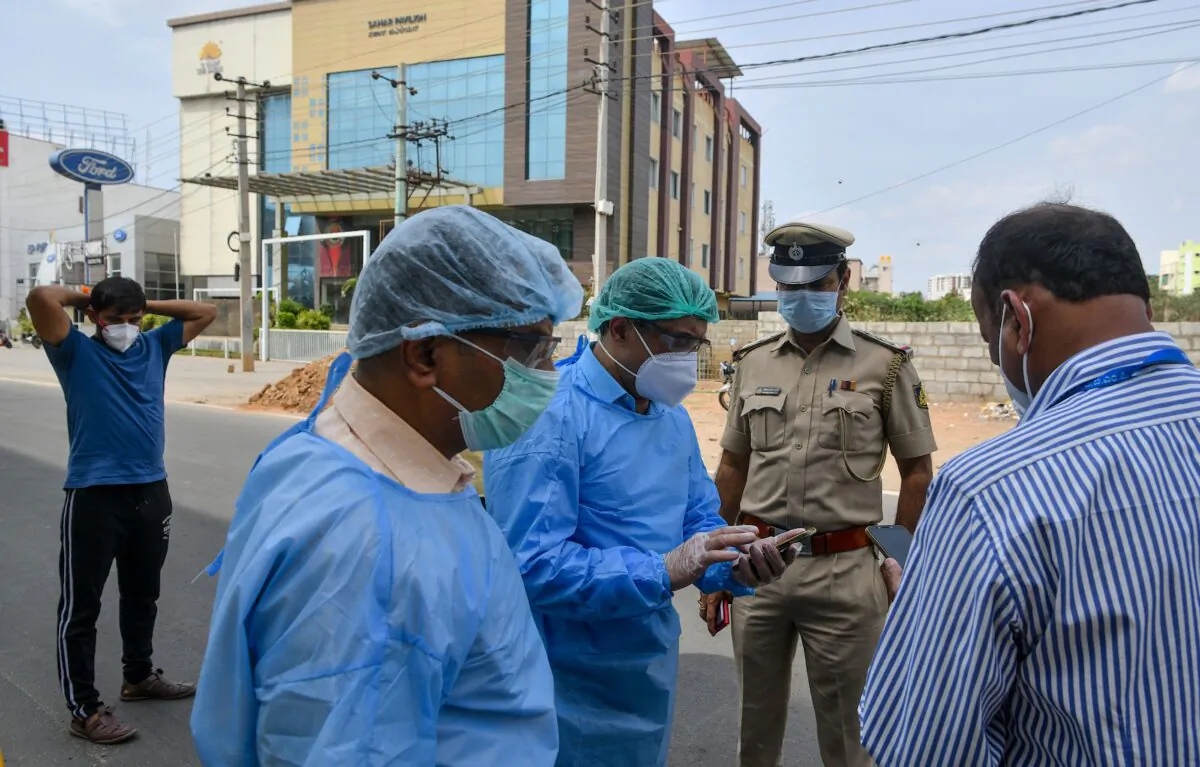 Paramedics, municipal, and police officials stand outside a private hotel as they plan the safe evacuation and hospitalisation of a suspected COVID-19 coronavirus customer that allegedly self-quarantined himself in the hotel, during the first day of a 21-day government-imposed nationwide lockdown as a preventive measure against the CCP virus in Bangalore on March 25, 2020. (Manjunath Kiran/AFP via Getty Images)