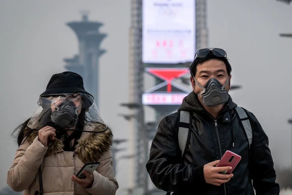 People wearing face masks walk at the Olympic park in Beijing on March 24, 2020. (Nicolas Asfouri/AFP via Getty Images)