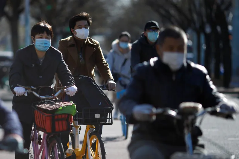 People wearing face masks ride bikes following an outbreak of the CCP Virus, in Beijing, China, March 27, 2020. (Reuters/Carlos Garcia Rawlins)