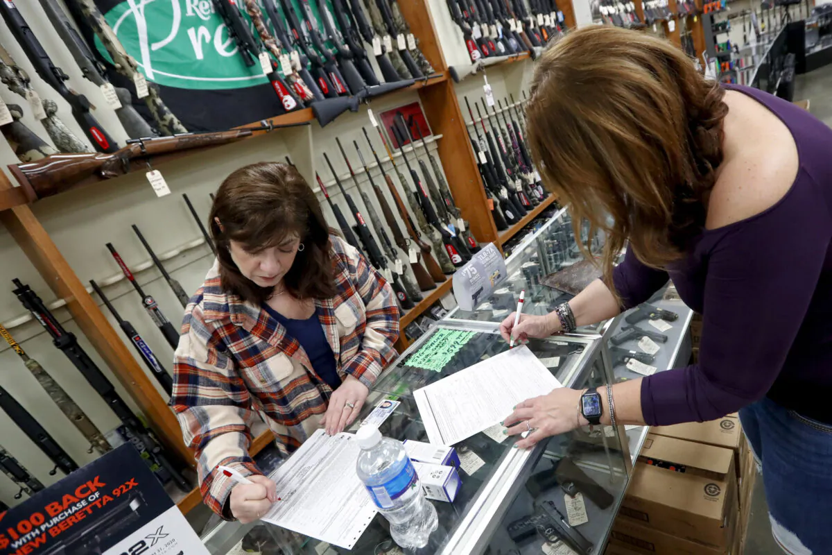 A woman fills out the buyer part of legal forms to buy a handgun as a shop worker (L) fills out the vendor’s portion at Dukes Sport Shop in New Castle, Pa., on March 25, 2020. (Keith Srakocic/AP Photo)