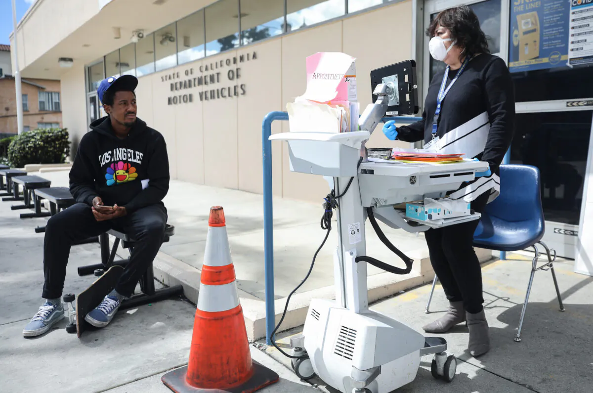 A Department of Motor Vehicles worker (R) speaks with a man who did not have an appointment at an appointment desk in front of the DMV building, with a cone used to implement social distancing in Los Angeles, California, on March 23, 2020. (Mario Tama/Getty Images)
