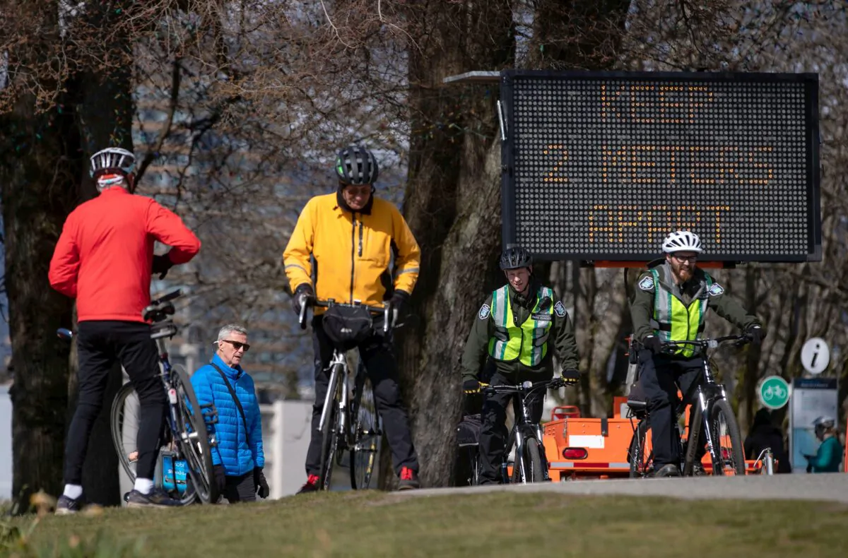 A sign warns people to keep at least 2 metres apart from one another due to concerns about the spread of COVID-19, as park rangers and others bike and walk on the seawall, in Vancouver on March 25, 2020. (The Canadian Press/Darryl Dyck)
