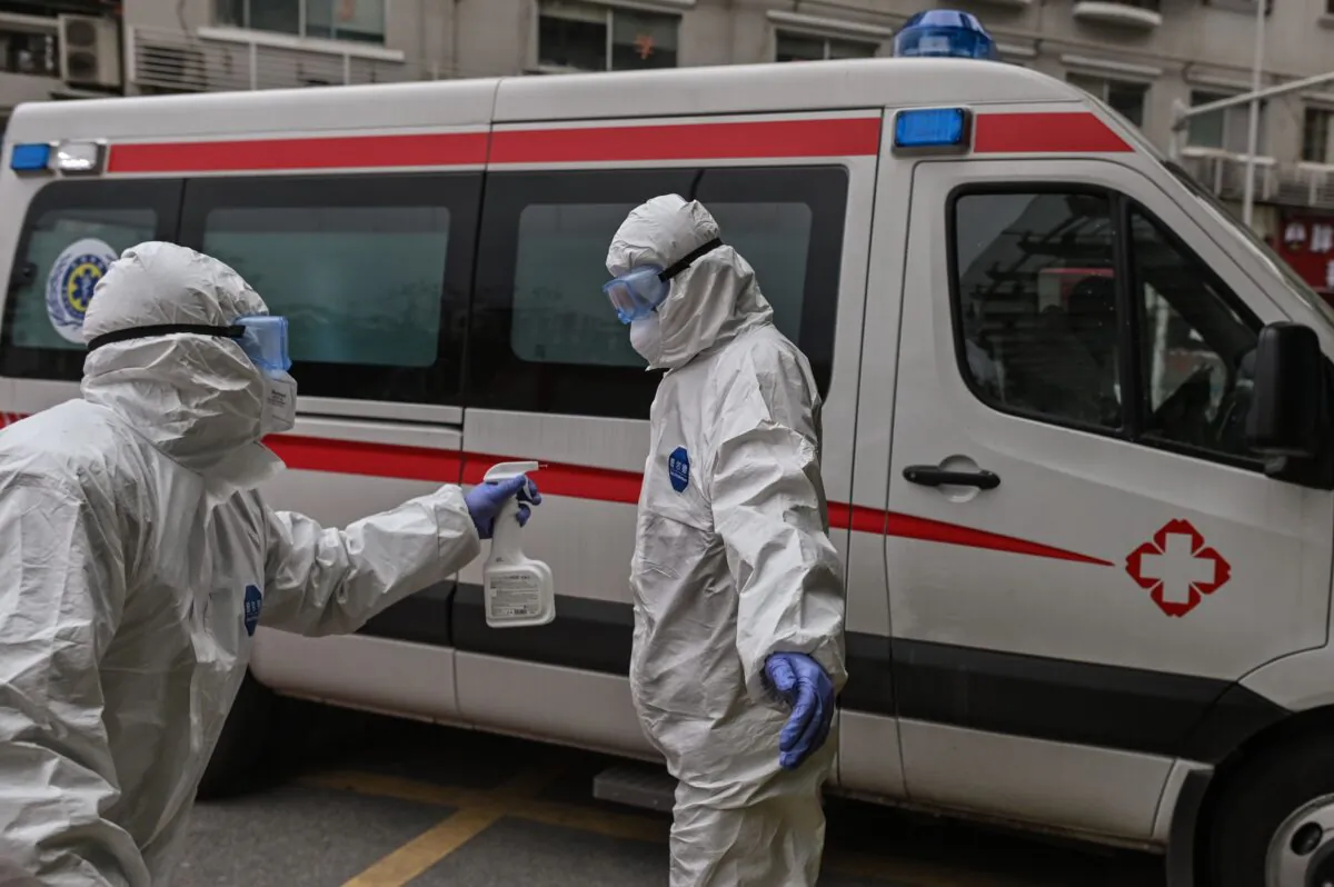 An ambulance medical staff sprays disinfectant on his colleague after they shipped a patient, who was cured from CCP Virus recently, at Wuhan Red Cross Hospital in Wuhan, China on March 30, 2020. (HECTOR RETAMAL/AFP via Getty Images)