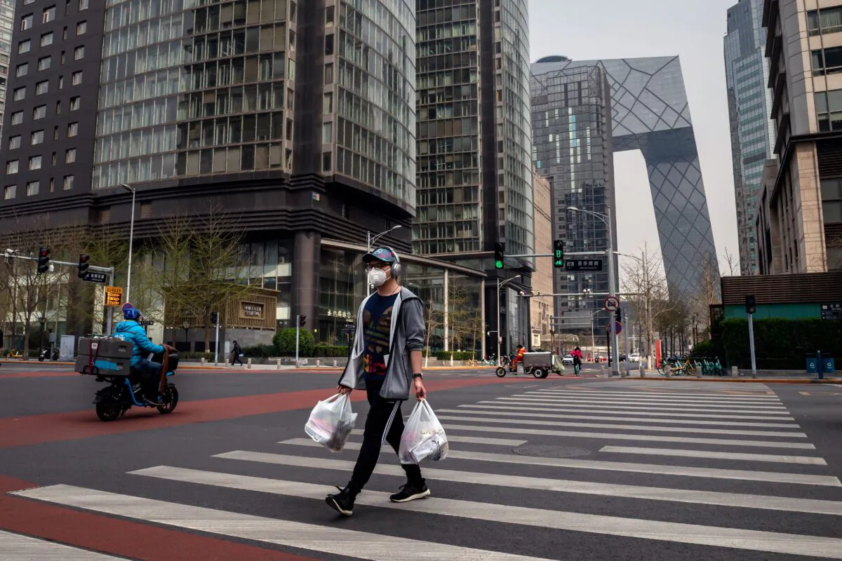 A man wearing a face mask amid the COVID-19 coronavirus outbreak crosses a street while carrying his groceries in Beijing, China, on March 30, 2020. (Nicolas Asfouri/AFP via Getty Images)