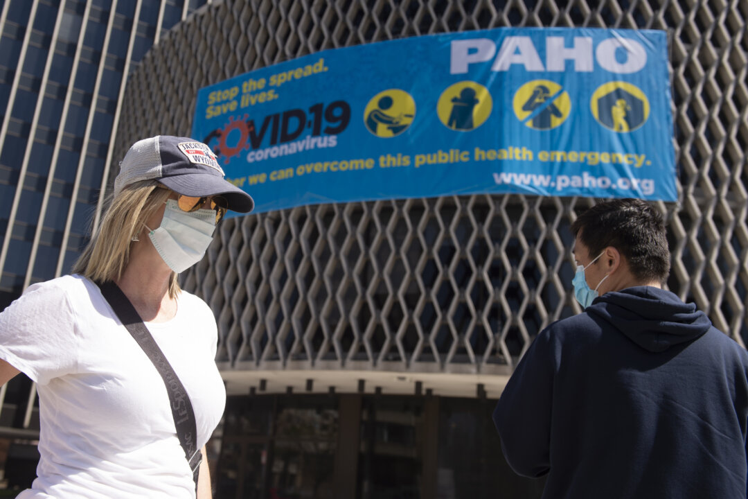 People wear masks as they walk past a CCP virus awareness sign outside the World Health Organization in Washington on March 30, 2020. (Andrew Caballero-Reynolds/AFP via Getty Images)