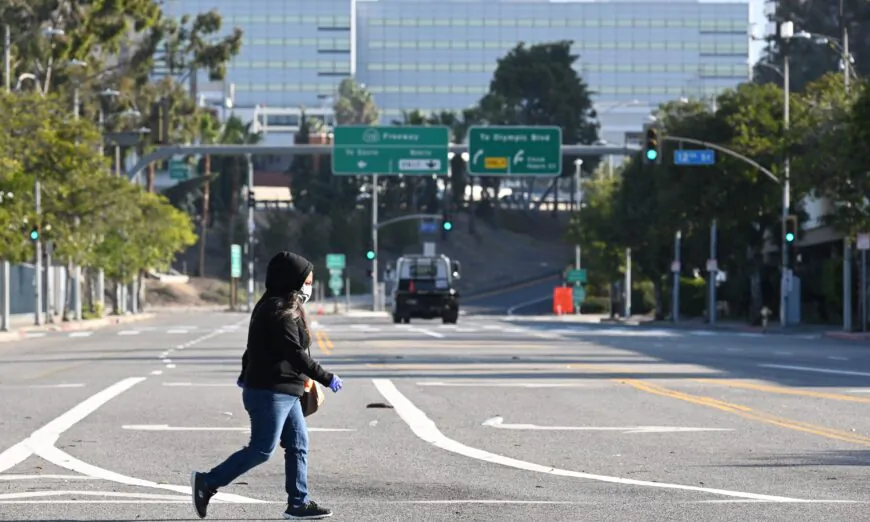 A woman wears a mask as she crosses an empty street near the Los Angeles Convention Center in downtown Los Angeles, California, on March 30, 2020. (Robyn Beck/AFP via Getty Images)