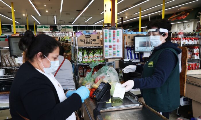 A shopper and cashier both wear masks and gloves and the cashier also has on a plastic visor at the checkout station Pat's Farms grocery store in Merrick, New York, on March 31, 2020. (Al Bello/Getty Images)