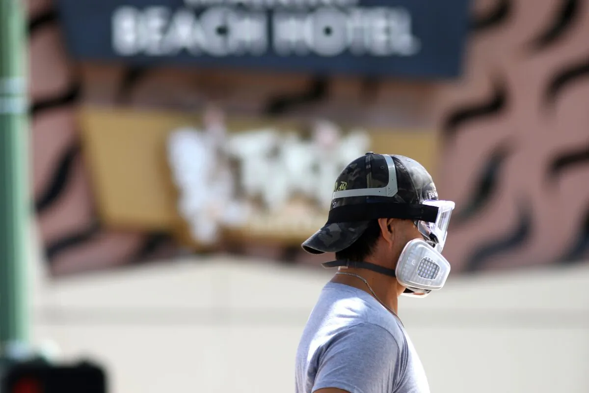 A man wears goggles and a mask as he walks a dog along Waikiki Beach in Honolulu on March 28, 2020. (Caleb Jones/AP Photo)