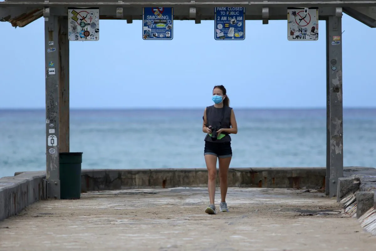 A woman wears a mask as she walks along a closed Waikiki Beach pier in Honolulu, Hawaii, on March 28, 2020. (Caleb Jones/AP Photo)