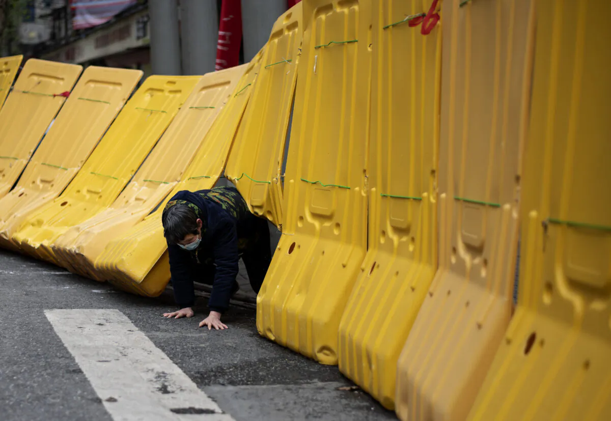A elderly woman crawls under a yellow barricade separating a residential compound in Wuhan, China on April 2, 2020. (NOEL CELIS/AFP via Getty Images)
