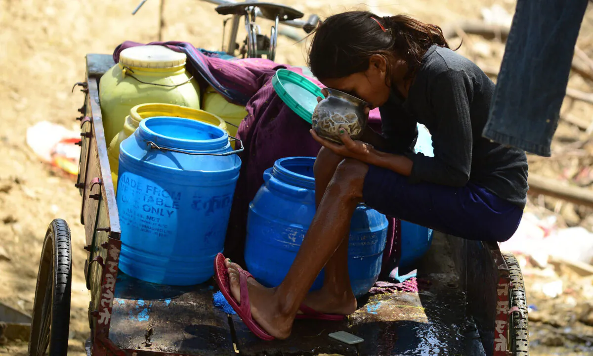 An Indian girl sits on a rickshaw trolley and drinks after collecting water in plastic barrels from a road side tap in Allahabad on March 22, 2016. (SANJAY KANOJIA/AFP via Getty Images)