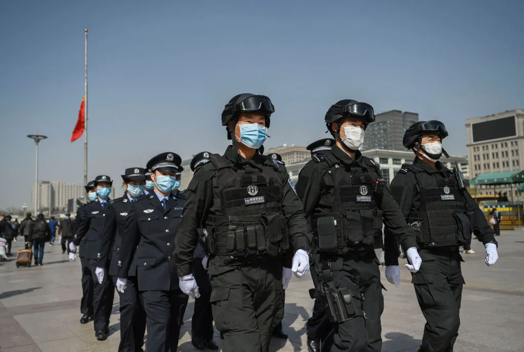 Chinese police officers wear protective masks as they march in formation away from a national flag at half staff after observing three minutes of silence to mark the country's national day of mourning for COVID-19 at Beijing Railway Station in Beijing on April 4, 2020. (Kevin Frayer/Getty Images)