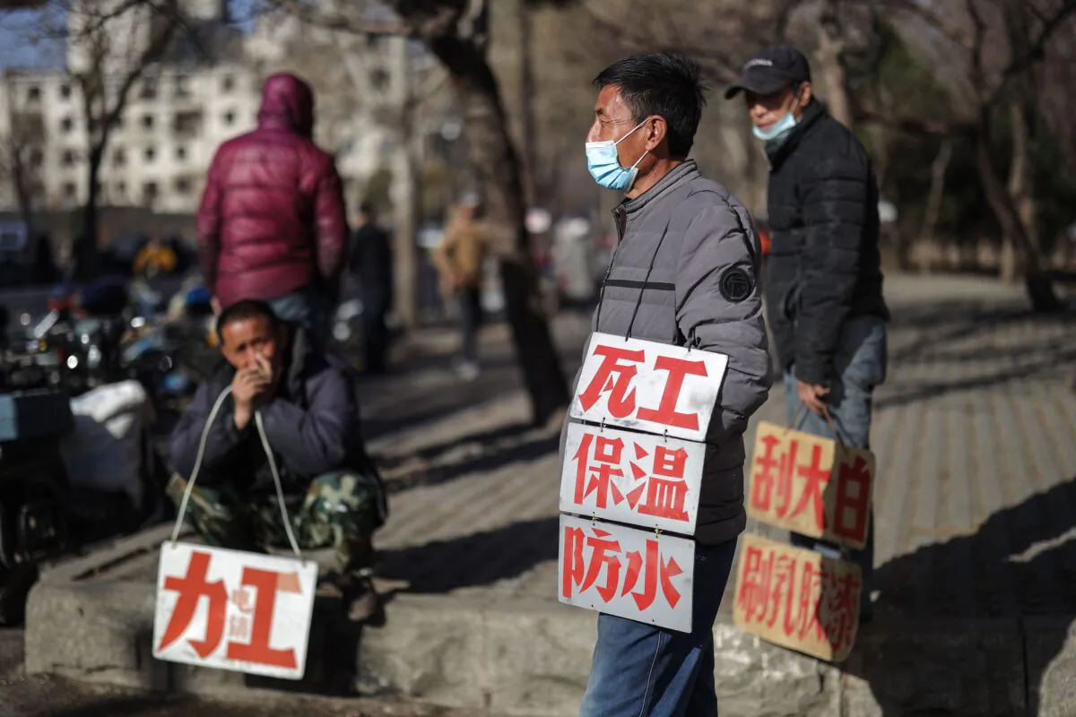 Day laborers hold signs advertising their skills as they wait to get hired for renovation work in Shenyang, China on March 27, 2020. (STR/AFP via Getty Images)
