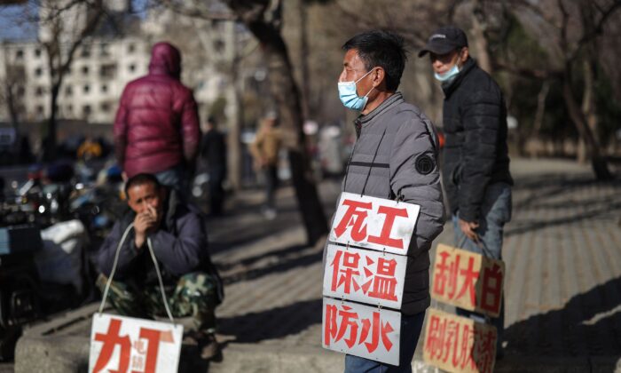 Day laborers hold signs advertising their skills as they wait to get hired for renovation work in Shenyang, China on March 27, 2020. (STR/AFP via Getty Images)