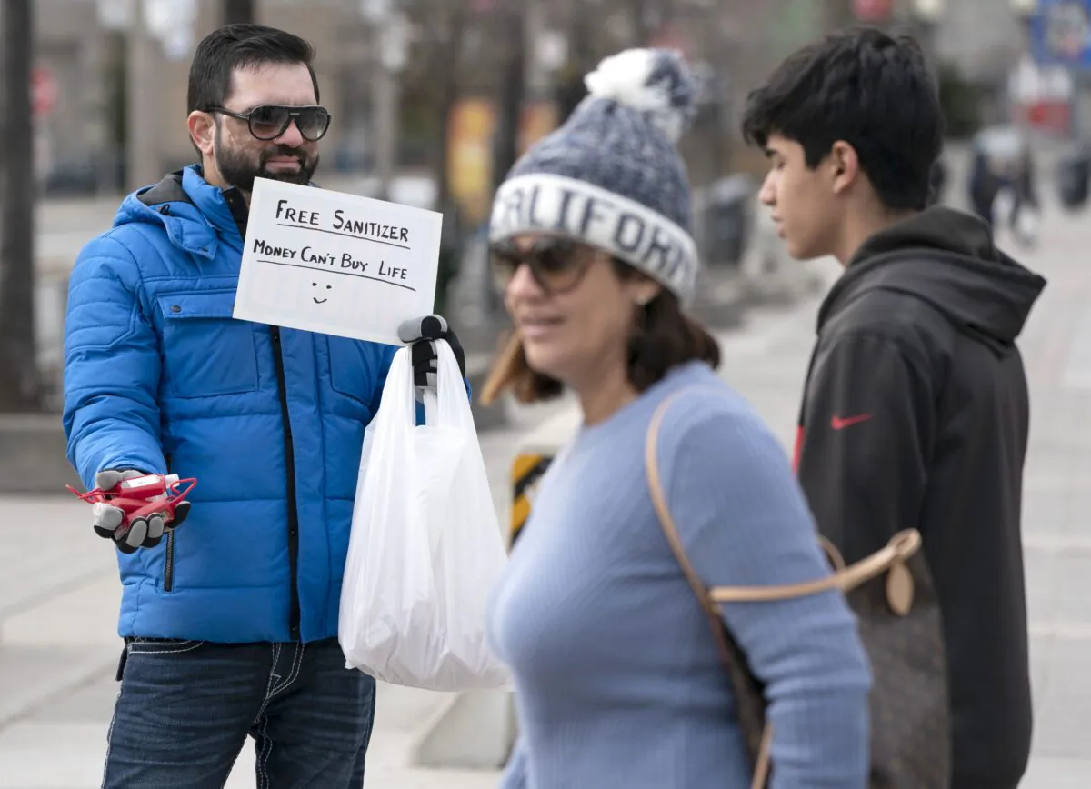 A man hands out free hand sanitizer at the base of the CN Tower in Toronto on March 14, 2020. (The Canadian Press/Frank Gunn)