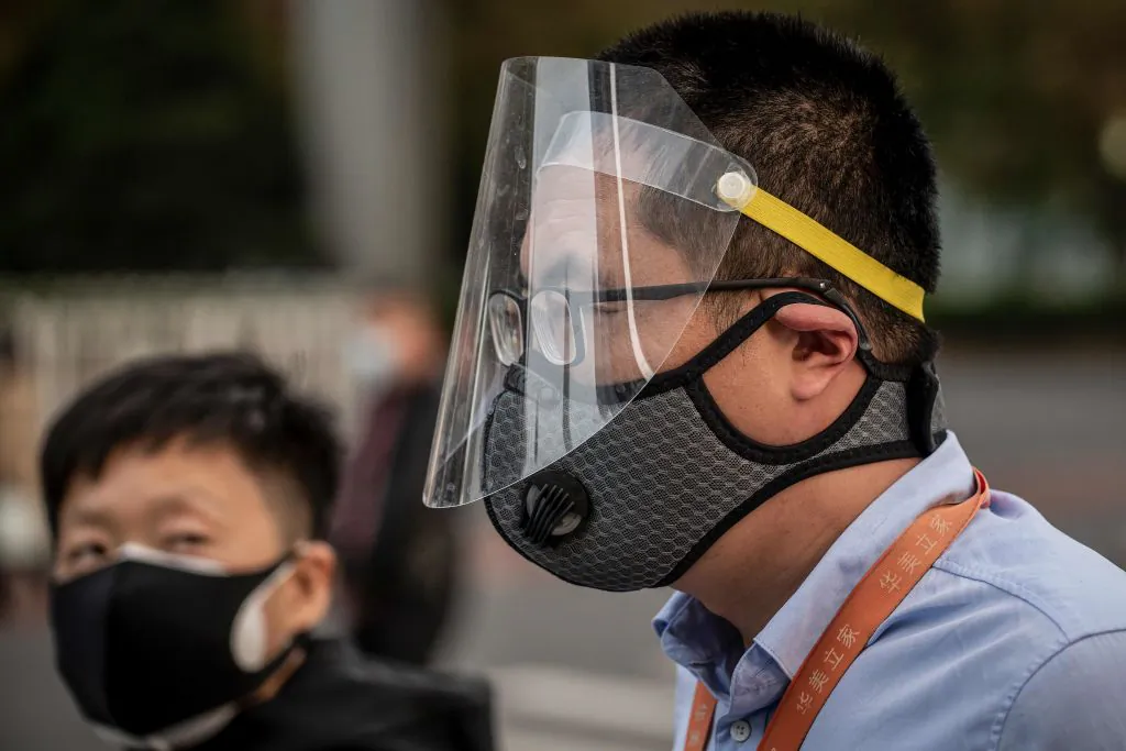 A man (R) wearing a facemask and a face shield commute on a street during rush hour in Beijing on April 7, 2020. (Nicolas Asfouri/AFP via Getty Images)