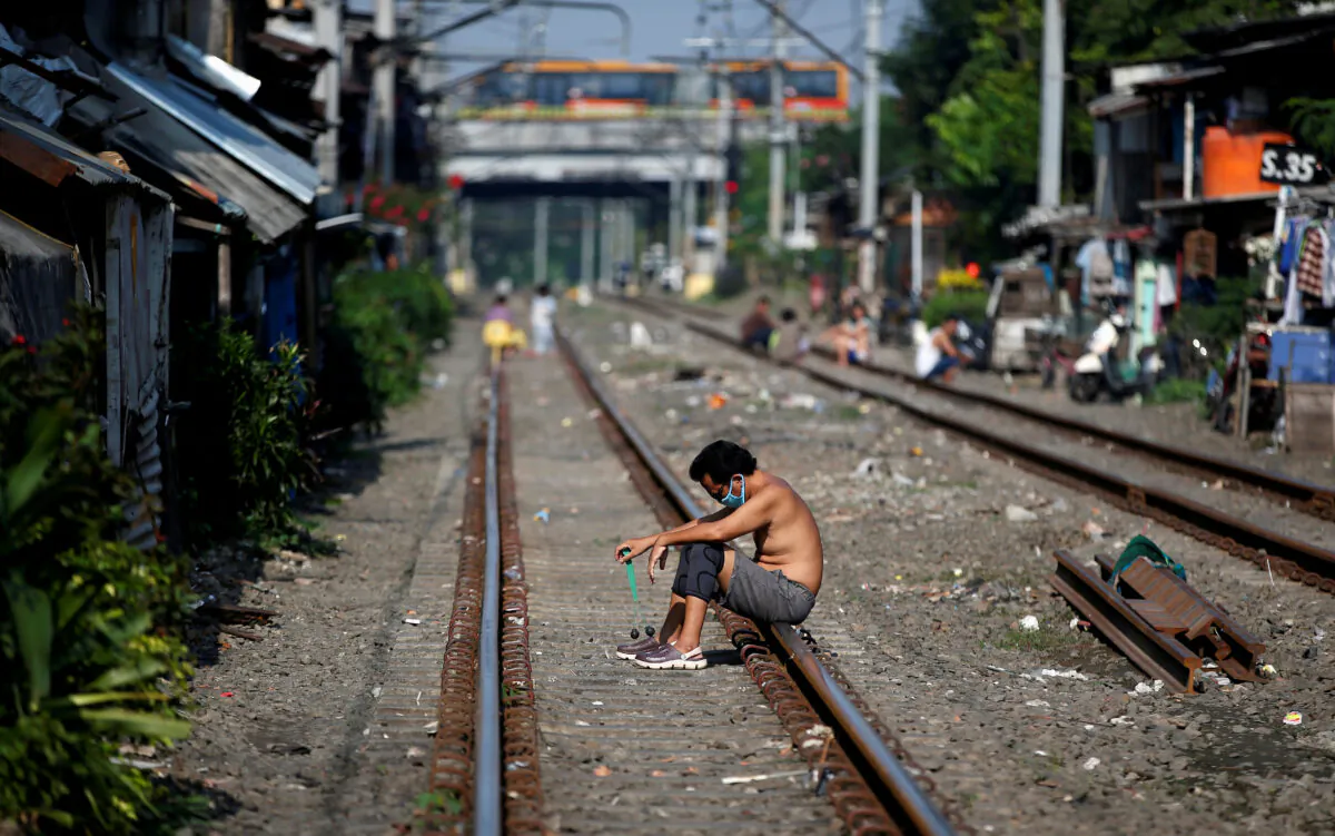 A man wears a protective mask as he sits along rail tracks during the large-scale social restrictions to prevent the spread of the CCP virus in Jakarta, Indonesia, on April 12, 2020. (Willy Kurniawan/Reuters)