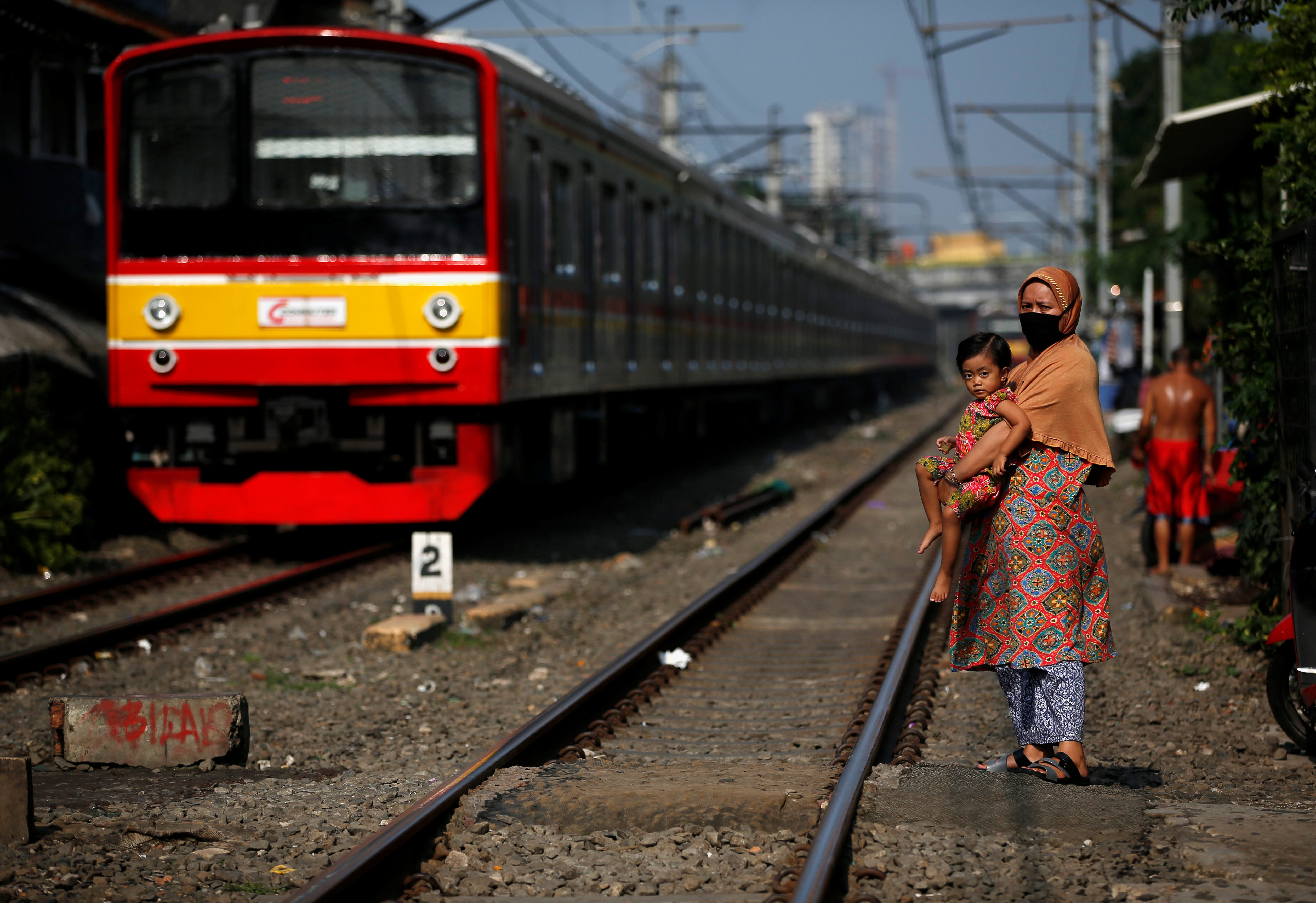A train passes next to a woman wearing a face mask and a child along rail tracks, during the large-scale social restrictions to prevent the spread of the CCP virus in Jakarta, Indonesia, on April 12, 2020.