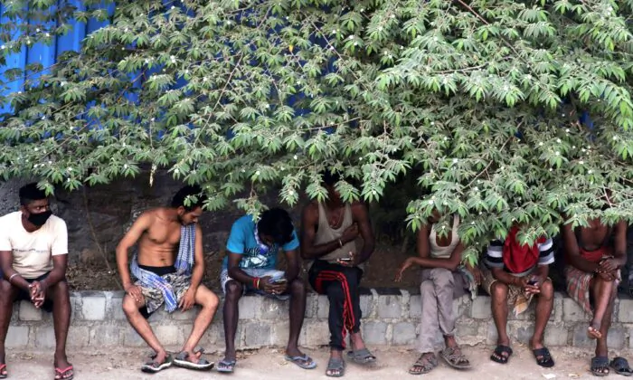 Migrant workers sit in the shade outside a slum area in Mumbai, India, on April 11, 2020. Social distancing has become the law in India, but in poor countries, observing social distancing is an option for only the better off. (AP Photo/Rajanish Kakade)