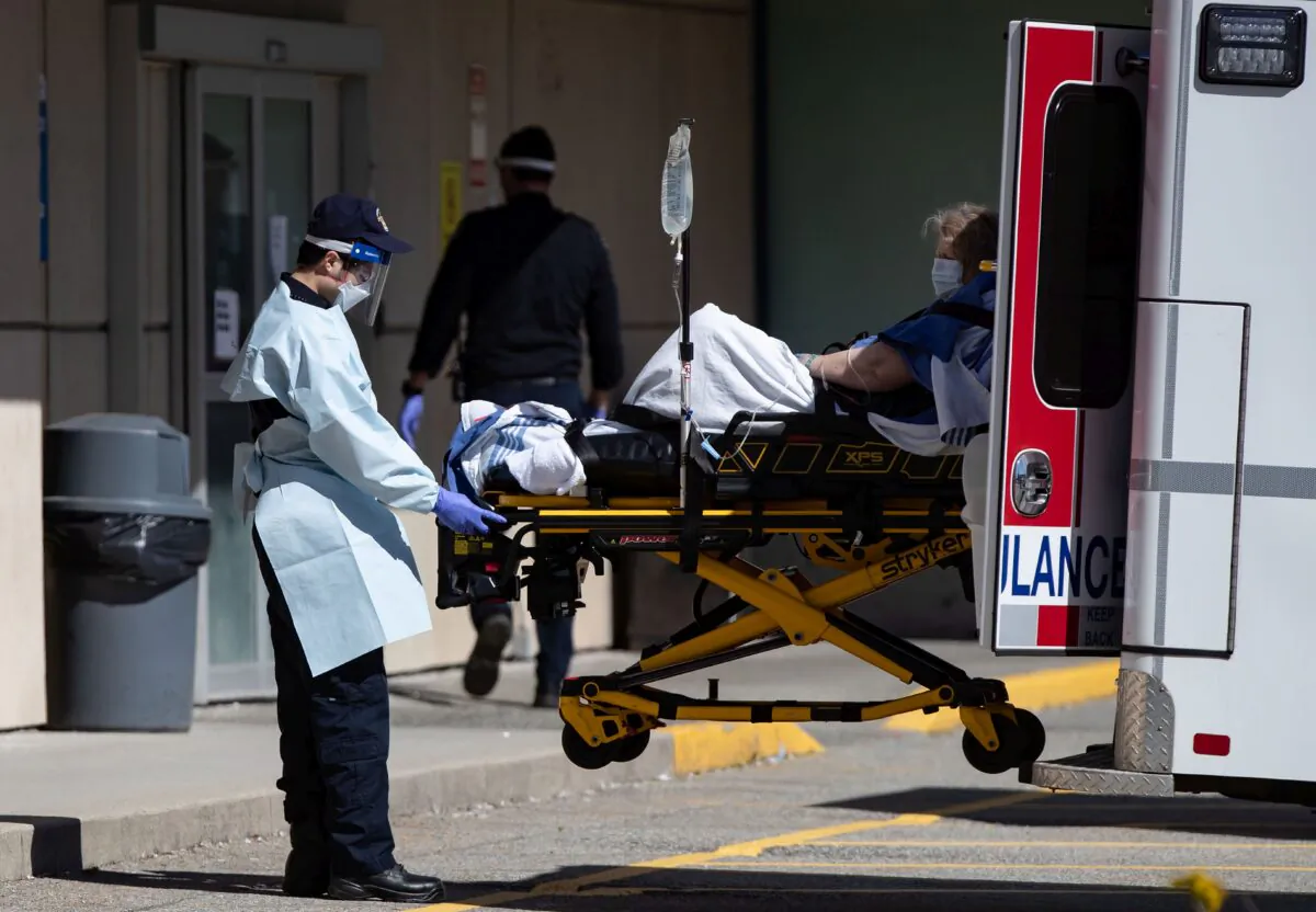 A B.C. Ambulance Service employee wearing protective gear moves a patient from an ambulance to the emergency department at Royal Columbian Hospital in New Westminster on April 12, 2020. (The Canadian Press/Darryl Dyck)
 